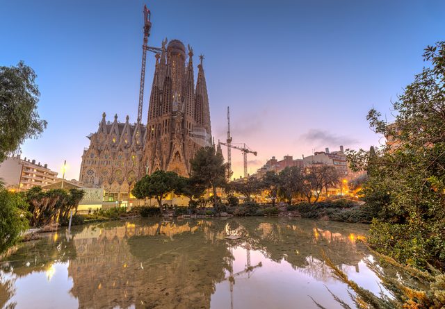 Alacakaranlıkta Barselona'daki Sagrada Família ve gölete yansıması